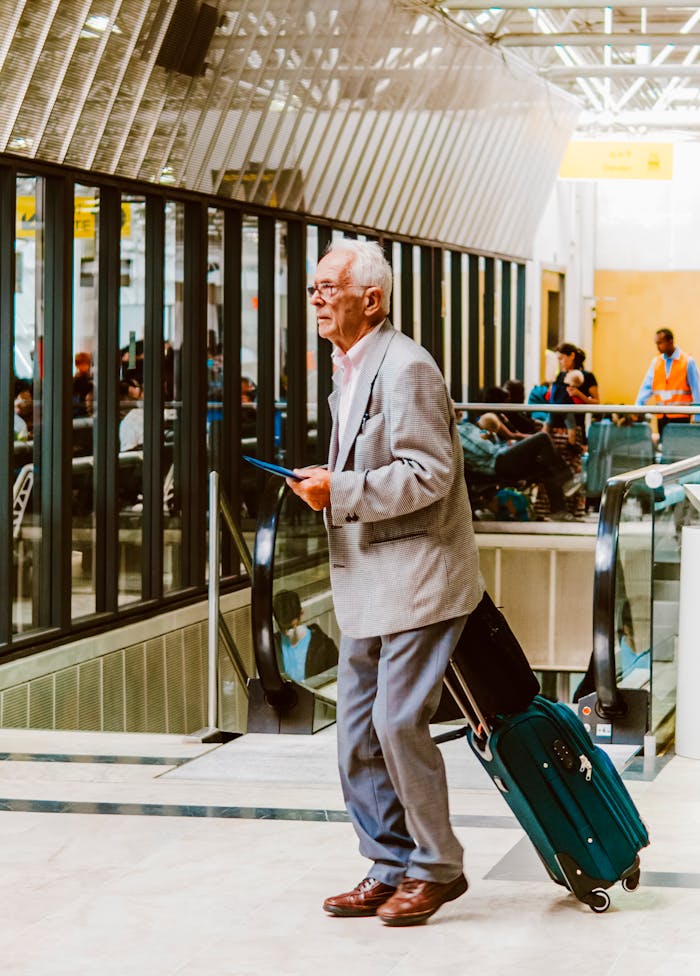 Senior man with suitcase and tablet walking through modern airport terminal.