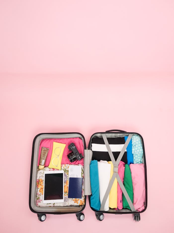Open suitcase with travel essentials neatly packed on a pink backdrop. Perfect for vacation planning.